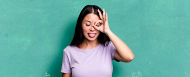 Güzel Latin kadın mutlu bir şekilde gülümsüyor, şaka yapıyor, gözetleme deliğinden bakıyor, sırları gözetliyor.