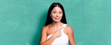 Güzel Latin bir kadın neşeyle gülümsüyor, mutlu hissediyor ve yan ve yukarı doğru işaret ediyor, fotokopi alanında nesneler gösteriyor.