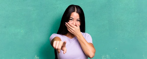 pretty latin woman laughing at you, pointing to camera and making fun of or mocking you