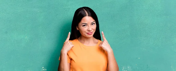 pretty latin woman with a bad attitude looking proud and aggressive, pointing upwards or making fun sign with hands