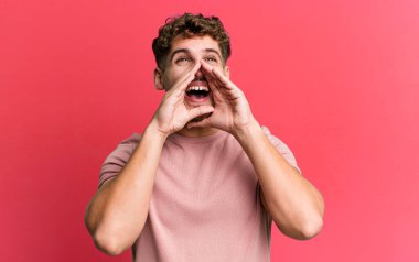 young adult caucasian man feeling happy, excited and positive, giving a big shout out with hands next to mouth, calling out