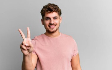 young adult caucasian man smiling and looking friendly, showing number two or second with hand forward, counting down