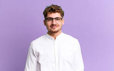 young adult caucasian man smiling positively and confidently, looking satisfied, friendly and happy