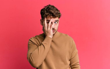 young adult caucasian man feeling bored, frustrated and sleepy after a tiresome, dull and tedious task, holding face with hand