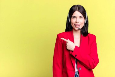 Neşeli bir şekilde gülümsüyor, mutlu hissediyor ve bir tarafı işaret ediyor. Kulaklık takan bir pazarlamacı.