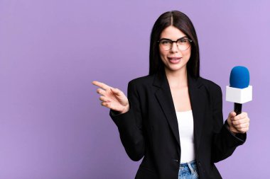 Neşeli bir şekilde gülümsüyor, mutlu hissediyor ve bir tarafı işaret ediyor. Mikro bilgisayarlı gazeteci ya da sunucu