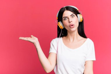 Şaşırmış ve şok olmuş bir şekilde, çenesi düşmüş bir şekilde elinde bir nesne tutarken. Bir kulaklığı dinlemek.