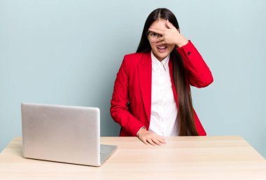 Güzel Asyalı kadın şok olmuş, korkmuş ya da korkmuş görünüyor. Yüzü elle kapatılmış. iş masası konsepti