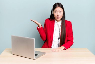 Güzel Asyalı kadın şaşırmış ve şok olmuş görünüyor. Çenesi düşmüş ve elinde bir nesne var. iş masası konsepti