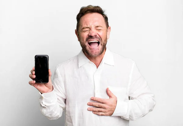 中年の男は陽気な冗談で大声で笑った スマートフォンを見せると — ストック写真