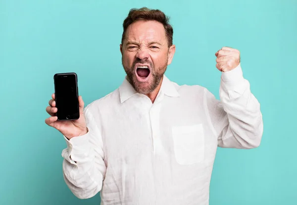 怒りの表情で積極的に叫ぶ中年男性 スマートフォンを見せると — ストック写真