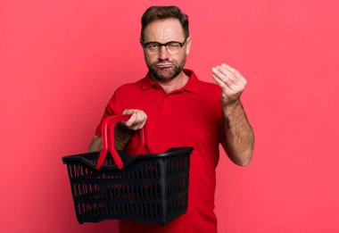 Orta yaşlı bir adam kapiş ya da para hareketi yapıyor, sana ödemeni söylüyor. boş alışveriş sepeti kavramı