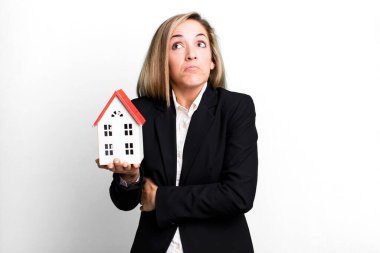 pretty blonde woman shrugging, feeling confused and uncertain. real state concept