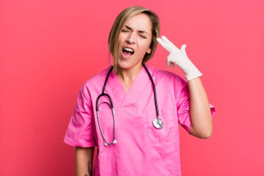 pretty blonde woman looking unhappy and stressed, suicide gesture making gun sign. nurse concept