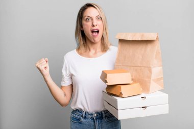 pretty blonde woman shouting aggressively with an angry expression. paper fast food take away packages