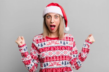 pretty blonde woman shouting aggressively with an angry expression. christmas and santa hat concept