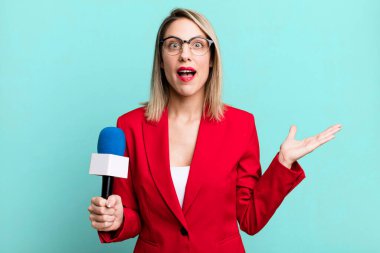pretty blonde woman feeling happy and astonished at something unbelievable. presenter or journalist with a microphone