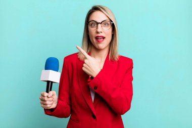 pretty blonde woman looking excited and surprised pointing to the side. presenter or journalist with a microphone