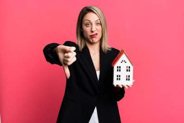 pretty blonde woman feeling cross,showing thumbs down. real state concept