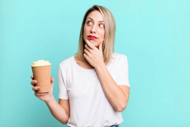 pretty blonde woman thinking, feeling doubtful and confused with a hot coffee