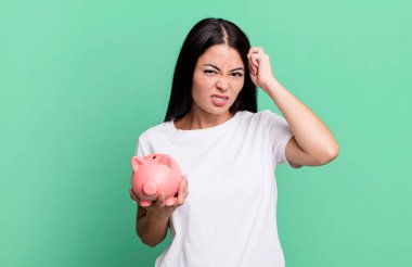 İspanyol güzel kadın şaşkın ve şaşkın hissediyor, domuz kumbarasıyla kafayı yediğini gösteriyor.