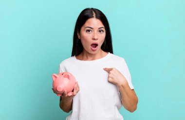 İspanyol güzel bir kadın ağzı açık, şaşkın ve şaşırmış görünüyor, domuz kumbarası ile kendini işaret ediyor.