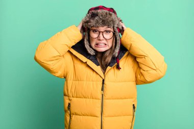 hispanic pretty woman feeling stressed, anxious or scared, with hands on head wearing anorak. cold and winter concept