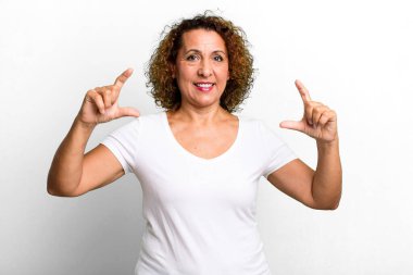 Orta yaşlı İspanyol bir kadın iki eliyle kendi gülümsemesini çiziyor, olumlu ve mutlu görünüyor, sağIık kavramı.