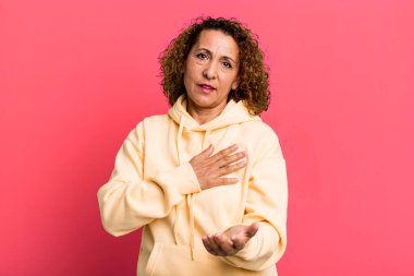 Orta yaşlı İspanyol bir kadın mutlu ve aşık, bir eli kalbinin yanında gülümsüyor ve diğer eli önde uzanıyor.