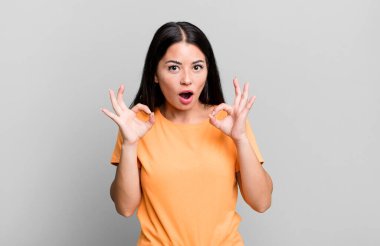 Güzel Latin bir kadın şok olmuş, şaşırmış ve şaşırmış hissediyor. Onaylıyor. İki eliyle işaret veriyor.