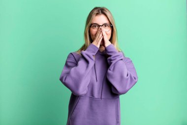 Sarışın, güzel bir kadın mutlu, neşeli, şanslı ve şaşkın görünüyor. İki eliyle ağzını kapatıyor.