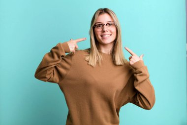 Sarışın, güzel bir kadın, kendine güvenerek gülümsüyor. Geniş bir gülümseme, pozitif, rahat, tatmin olmuş bir tavır.