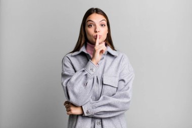 pretty young adult woman looking serious and cross with finger pressed to lips demanding silence or quiet, keeping a secret
