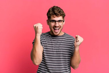 young adult caucasian man feeling happy, positive and successful, celebrating victory, achievements or good luck