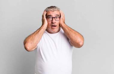 Orta yaşlı bir adam mutsuz, korkmuş ya da endişeli görünüyor ağzı sonuna kadar açık ve iki kulağını da elleriyle kapatıyor.