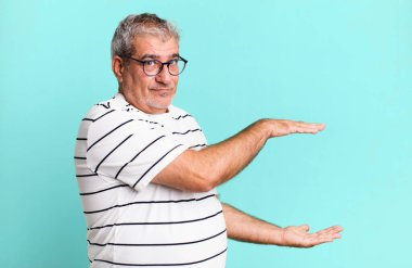 Orta yaşlı bir adam bir objeyi iki eliyle fotokopi alanında tutuyor, bir objeyi gösteriyor, sunuyor ya da reklamını yapıyor.