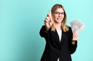 young pretty woman smiling proudly and confidently making number one. business and money concept