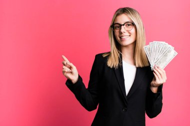 young pretty woman smiling cheerfully, feeling happy and pointing to the side. business and money concept