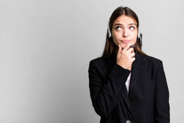 Genç, güzel bir kadın düşünüyor, kuşkulu ve şaşkın hissediyor. tele pazarlama aracı konsepti