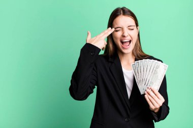 Genç ve güzel bir kadın mutsuz ve stresli görünüyor, intihar jesti silah işareti yapıyor. iş ve dolar banknotları kavramı