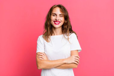 Genç, güzel bir kadın mutlu, gururlu ve tatmin olmuş görünüyor. Kollarını kavuşturup gülümsüyor.