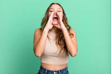 Genç, güzel bir kadın mutlu, heyecanlı ve pozitif hissediyor. Elleri ağızda, bağırıyor.