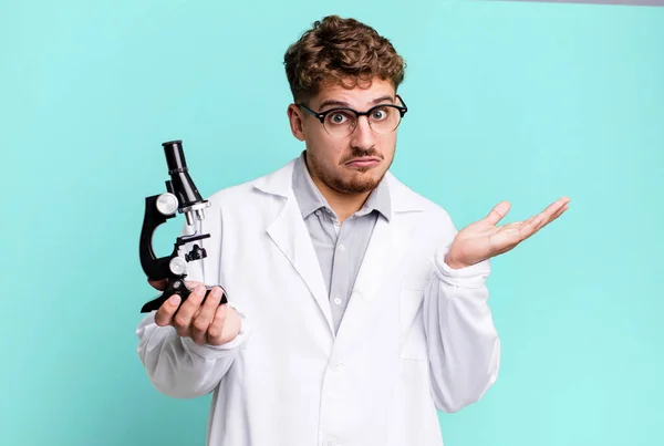 young adult caucasian man feeling puzzled and confused and doubting. scients laboratory student with a microscope concept