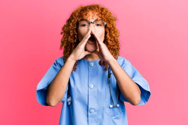 Kızıl saçlı, güzel bir kadın, mutlu hissediyor, elleri ağzının kenarında bağırıyor. hemşire konsepti