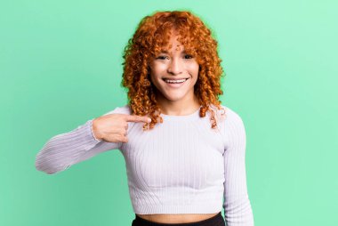 kızıl saçlı güzel kadın mutlu, gururlu ve şaşırmış görünüyor, neşeli bir şekilde kendini gösteriyor, kendinden emin ve yüce hissediyor.