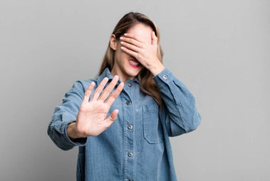 Yüzünü eliyle kapatıyor ve kamerayı durdurmak için diğer elini öne koyuyor, fotoğraf ya da resimleri reddediyor.