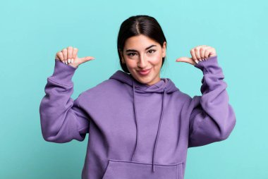 Gururlu, kibirli ve kendinden emin, tatmin olmuş ve başarılı görünüyor, kendini işaret ediyor.