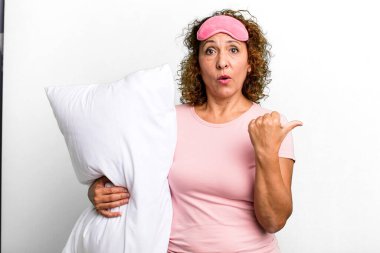 pretty middle age woman looking astonished in disbelief wearing pajamas night wear and a pillow