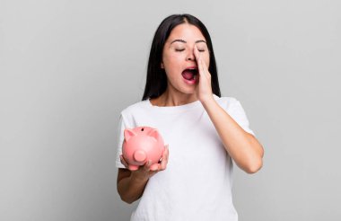 İspanyol güzel kadın kendini mutlu hissediyor, domuz kumbarasıyla elleri ağızda bağırıyor.