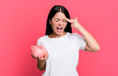 İspanyol güzel kadın mutsuz ve stresli görünüyor, intihar jesti domuz kumbarasıyla silah işareti yapıyor.